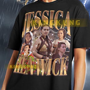 Può includere: Maglietta nera con una stampa grafica dorata di una donna con una spada e il testo "Jessica Kenwick".