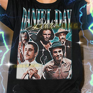 May include: Black t-shirt featuring a graphic of Daniel Day-Lewis and the text "DANIEL DAY LEWIS". The design includes images of the actor in various roles. The shirt is worn by a person.
