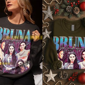May include: Two sweatshirts, one dark gray and one olive green, each featuring a graphic of several women and the name "BRUNA MARQUEZINE" in a retro font. The dark gray sweatshirt is being worn, while the olive green one is displayed on a wooden surface with holiday decorations.