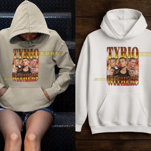 May include: A beige hoodie and a white hoodie are displayed. Both hoodies feature a graphic with the text "TYRIO KUNG WITHERS" in a stylized font, along with images of a person. The hoodies have a front pocket and a hood.