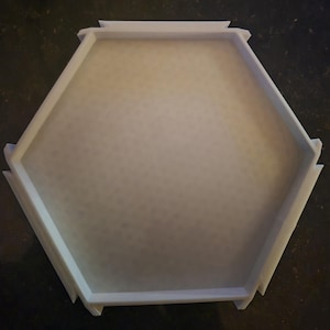 May include: A white, hexagonal tray with a textured interior. The tray has a raised edge and is made of a solid material. The tray's design is simple and modern, suitable for various uses.