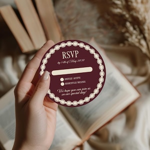 May include: A burgundy RSVP card with white lace trim and text. The card includes the text "RSVP by 14th of May 2030", a line for a name, and options to accept or decline. The card also includes the text "We hope you can join us on our special day!"