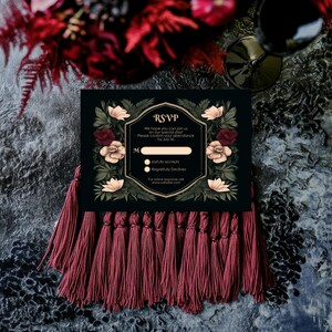 May include: Black RSVP card with gold trim and floral design. The card has a tassel border and the text "RSVP" in gold lettering. The text reads "We hope you can join us on our special day. Please confirm your attendance by July [blank space]" with two options: "joyfully accepts" and "Regretfully Declines". The card also includes the text "For online response visit www.website.com".