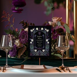 May include: A black wedding invitation with white floral illustrations and gold lettering. The invitation reads "Josephine & Adrian" and "Aug 13, 2023".