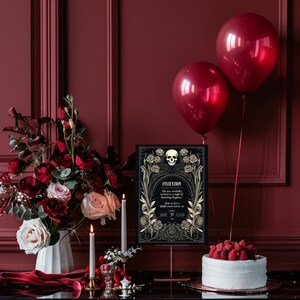May include: A black and gold Halloween invitation with a skull and floral design. The invitation is on a stand with a white cake decorated with raspberries and red balloons in the background.