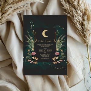 May include: A black wedding invitation with gold and green accents. The invitation features a crescent moon, floral illustrations, and the text "Celine & Isaac" and "together with their families invite you to the celebration of their wedding".