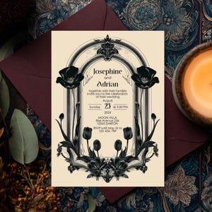 Op de afbeelding: Een uitnodigingskaart voor een bruiloft met een bloemenontwerp. De kaart toont de namen "Josephine en Adrian" en evenementdetails. Zwarte bloemelementen omlijsten de tekst op een crèmekleurige achtergrond. De kaart ligt op een bordeauxrode envelop.