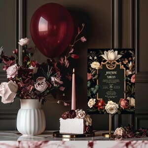 May include: A black and gold wedding invitation with floral designs and the text "Josephine and Adrian" in a gold frame. The invitation is on a gold stand with a white cake and a pink candle in the background.