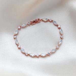 May include: A delicate rose gold bracelet with a chain adorned with clear oval-shaped stones and smaller round stones.
