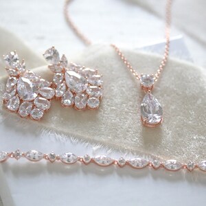 May include: A rose gold bridal jewelry set with a teardrop pendant necklace, matching earrings, and a bracelet. The set features clear cubic zirconia stones.