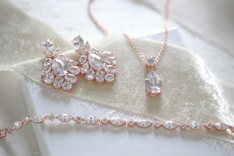 May include: A rose gold bridal jewelry set with a teardrop pendant necklace, matching earrings, and a bracelet. The set features clear cubic zirconia stones.