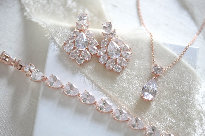 May include: A rose gold bridal jewelry set with a necklace, bracelet, and earrings. The set features clear cubic zirconia stones in a teardrop and round shape.