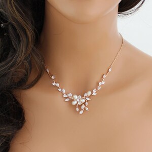 May include: A rose gold necklace with a delicate floral design featuring clear cubic zirconia stones and white pearls. The necklace is perfect for a wedding or other special occasion.