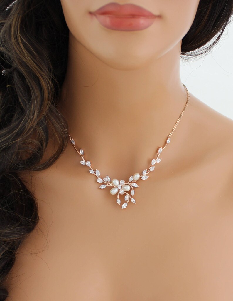 May include: A rose gold necklace with a delicate floral design featuring clear cubic zirconia stones and white pearls. The necklace is perfect for a wedding or other special occasion.