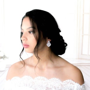 May include: A woman with long black hair wearing a white off-the-shoulder lace dress and sparkling crystal earrings.