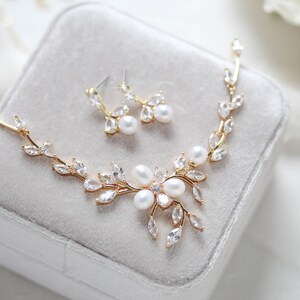 May include: A gold necklace and earrings set with a delicate leaf design and pearl accents. The necklace features a floral motif with multiple pearls in the center.