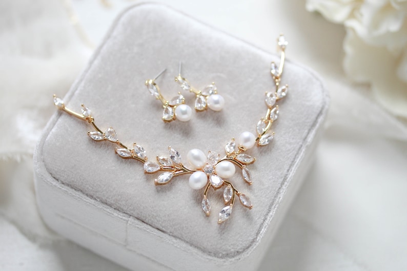 May include: A gold necklace and earrings set with a delicate leaf design and pearl accents. The necklace features a floral motif with multiple pearls in the center.