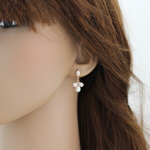 May include: Gold dangle earrings with a pearl and clear stones. The earrings are on a mannequin's ear.