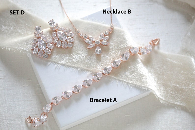 May include: A set of rose gold jewelry featuring a necklace, bracelet, and earrings. The necklace and earrings have a floral design with clear cubic zirconia stones. The bracelet has a simple design with clear cubic zirconia stones.