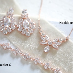May include: A rose gold bridal jewelry set with a necklace, earrings, and bracelet. The set features a delicate floral design with sparkling clear stones. The necklace is labeled "Necklace B", the earrings are labeled "SET E", and the bracelet is labeled "Bracelet C".