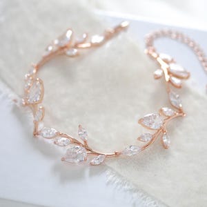 Puede incluir: Un delicado brazalete de oro rosa con un diseño de hojas adornado con piedras de circonita cúbica transparentes. El brazalete es ajustable y tiene una cadena delicada.