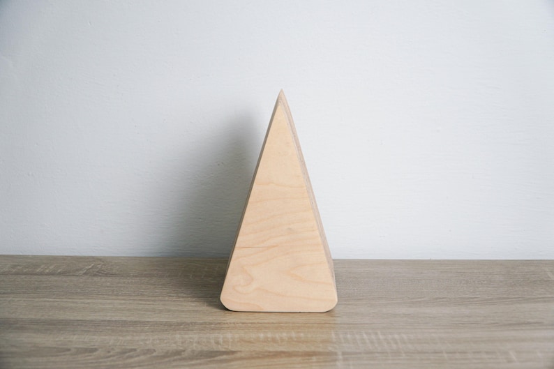 May include: A light wood triangular shaped geometric ornament. The ornament is made of wood and has a smooth, natural finish.
