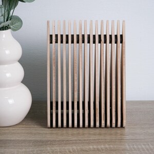 May include: A wooden slatted decorative object with a natural wood finish. The object is standing on a light brown surface.