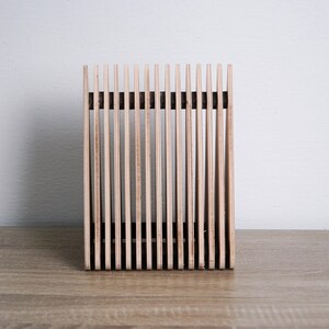 May include: A wooden magazine rack with a slatted design. The rack is made of natural wood and has a rectangular shape.