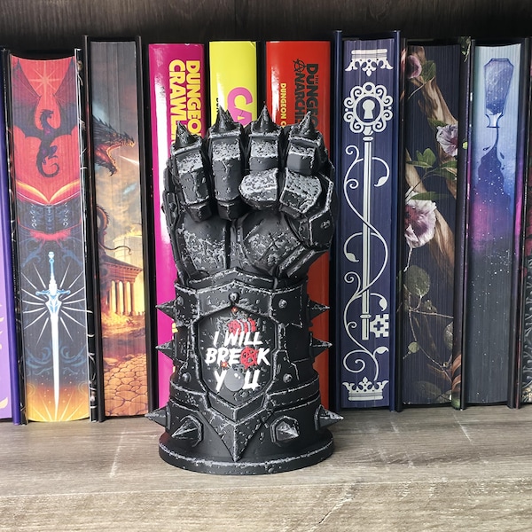 May include: A black, armored gauntlet sculpture featuring a clenched fist with spiked knuckles and a wrist plate. The center of the wrist plate displays the white text "I WILL BREAK YOU" with a small red bomb icon integrated into the lettering.