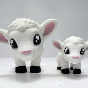 May include: Two white lamb figurines with large, expressive eyes and pink accents on their ears and noses. The lambs have black hooves and a textured, fluffy appearance, suggesting a 3D-printed design. One is larger than the other.