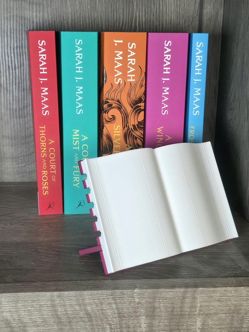 May include: A collection of colorful books by Sarah J. Maas, with titles including "A Court of Thorns and Roses" and "A Mist and Fury." The books are arranged vertically, with an open book in the foreground.