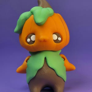 May include: A 3D-printed figurine of a pumpkin-headed character with large, expressive eyes. The figure has an orange head, green leafy collar, brown body, and small arms. The background is a solid purple.
