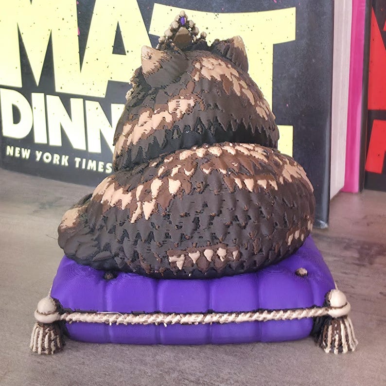 Peut inclure: Figurine de hibou brun couronn&eacute;, pos&eacute; sur un coussin violet avec une bordure en corde blanche et des glands. Le hibou pr&eacute;sente un motif de plumes d&eacute;taill&eacute; en marron et beige. Objet d&eacute;coratif.