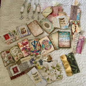 May include: A collection of assorted paper ephemera including rectangular tags, bookmarks with metal charms, and small cards featuring vintage-style floral, botanical, and abstract prints, lace trim, postage stamps, and layered paper textures.