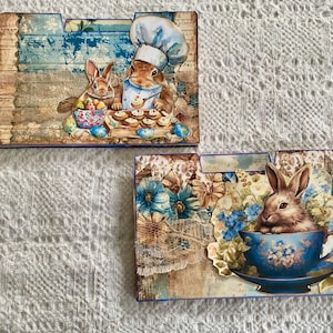 May include: Two sets of decorative file folders with a spring theme. The top folder features two bunnies baking cupcakes. The bottom folder features a bunny drinking tea from a blue and white teacup.