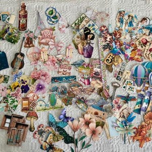 May include: A collection of colorful paper cutouts featuring various designs, including flowers, butterflies, musical instruments, and miniature furniture. The assortment includes a bottle, a guitar, and hot air balloons, all arranged on a textured white surface.