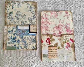 May include: Two decorative paper envelopes with floral patterns. The top envelope has a blue and white floral pattern. The bottom envelope has a pink and white floral pattern. Both envelopes have a scalloped edge.