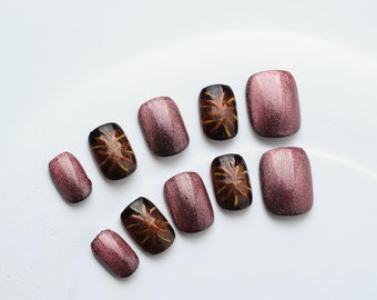 May include: Set of ten false nails with a burgundy shimmer finish and a brown and gold swirl design.