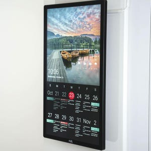 Peut inclure: Un calendrier numérique à cadre noir affiche une vue panoramique d'un lac avec des bateaux et un quai. L'écran affiche la date, l'heure et un calendrier pour octobre 2024. Le calendrier comprend le texte "FLEX".