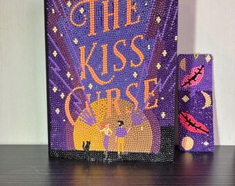 以下が含まれることがあります： エリン・スターリング著『The Kiss Curse』のダイヤモンドアートブックカバー。紫色の背景にオレンジ色の文字、大きな黄色い月、2人の人物、黒猫が描かれています。隣には、ピンクの唇と月のモチーフが施されたお揃いの長方形のしおりが置かれています。