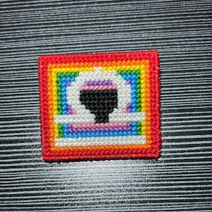 Könnte beinhalten: Ein quadratischer Stickaufnäher mit einem zentralen weißen Waage-Sternzeichen-Symbol mit schwarzer Mitte. Das Design ist von konzentrischen quadratischen Rändern in leuchtenden Regenbogenfarben umgeben, darunter Rot, Orange, Gelb, Grün, Blau und Violett.
