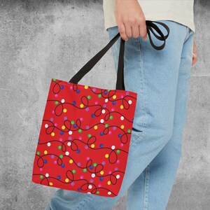 May include: A red tote bag with a pattern of colorful string lights on a black wire. The bag has black handles.
