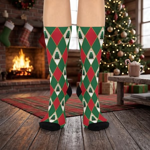 May include: A pair of crew socks featuring a repeating argyle pattern in shades of green and red. The design includes white diamond shapes containing small green Christmas tree illustrations. The socks have solid black toe and heel sections.