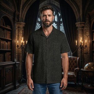 K&ouml;nnte beinhalten: Ein dunkelgr&uuml;nes kurz&auml;rmeliges Hemd mit Spinnennetz-Muster. Das Hemd hat einen Camp-Kragen und wird mit einer blauen Jeans getragen. Der Hintergrund zeigt eine Bibliothek mit B&uuml;cherregalen, Kerzen und einem Ledersessel.