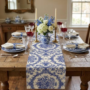May include: A dining table set for a formal meal. The table is adorned with a blue and white floral patterned runner, matching plates, and a vase of flowers. Tall candles and wine glasses complete the elegant setting.