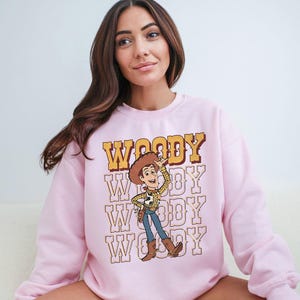 a woman sitting on a couch wearing a pink woody sweatshirt