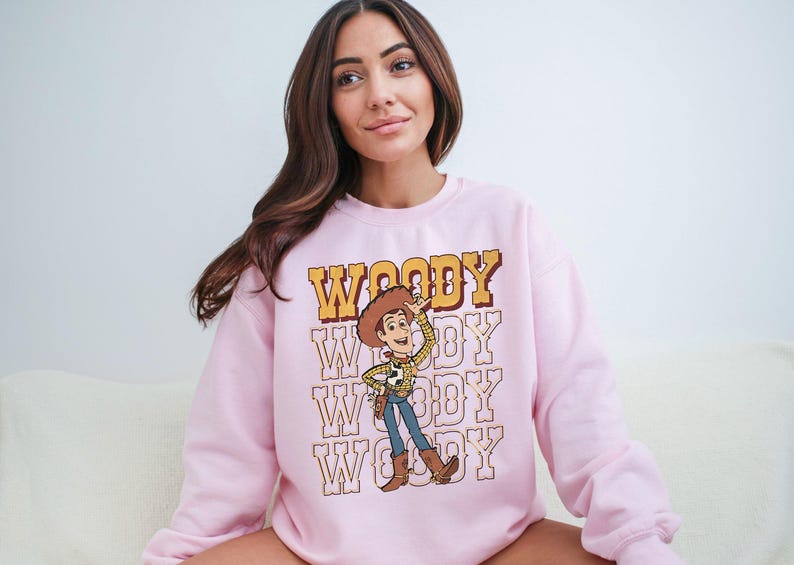 a woman sitting on a couch wearing a pink woody sweatshirt