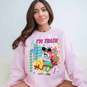 a woman sitting on a couch wearing a pink sweatshirt