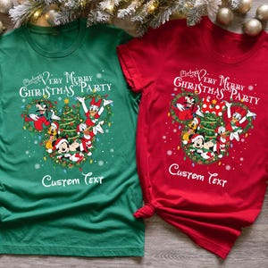 May include: Two short-sleeved t-shirts, one green and one red, featuring a festive design. The shirts display a Mickey Mouse-themed Christmas graphic with the text "Mickey's Very Merry Christmas Party" and space for custom text.