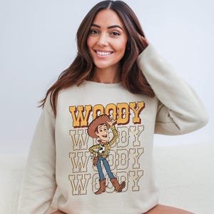 a woman sitting on a couch wearing a woody sweatshirt